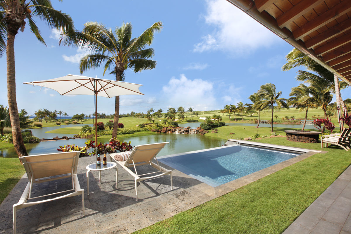 Luxurious tropical pool setting off lanai with two lounge chairs and umbrella. View over golf course lakes and fairway to ocean. 