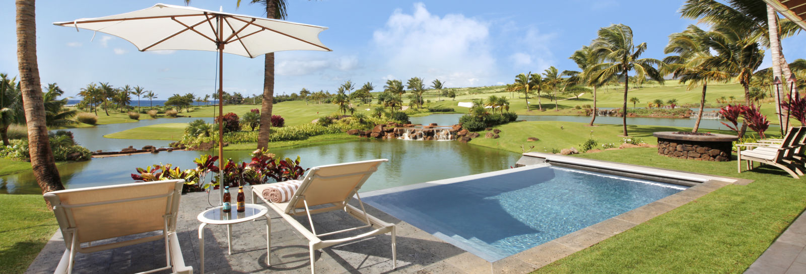 Luxurious tropical pool setting off lanai with two lounge chairs and umbrella. View over golf course lakes and fairway to ocean. 