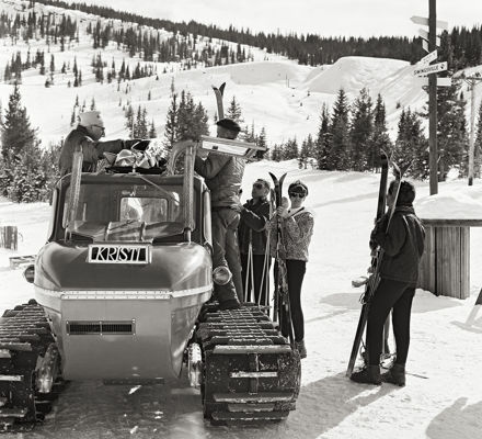 Black and white photo of skiiers getting into a snowmobile