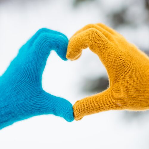 Photo of two hands wear gloves yellow blue show gesture sign heart symbol love romantic feelings affection outdoors